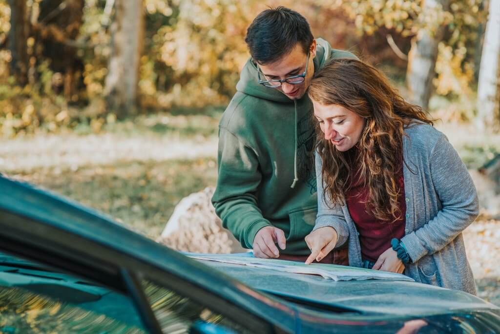 Maps & Guides a couple reading a map that's spread out on the hood of a car